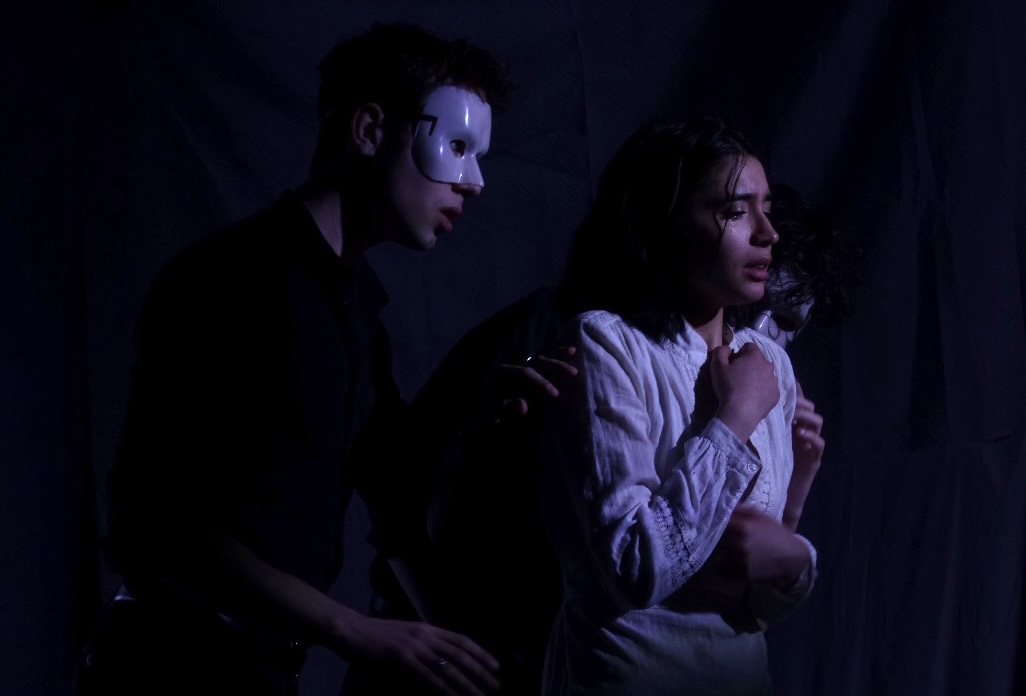 A masked figure beside Julia in low blue light.