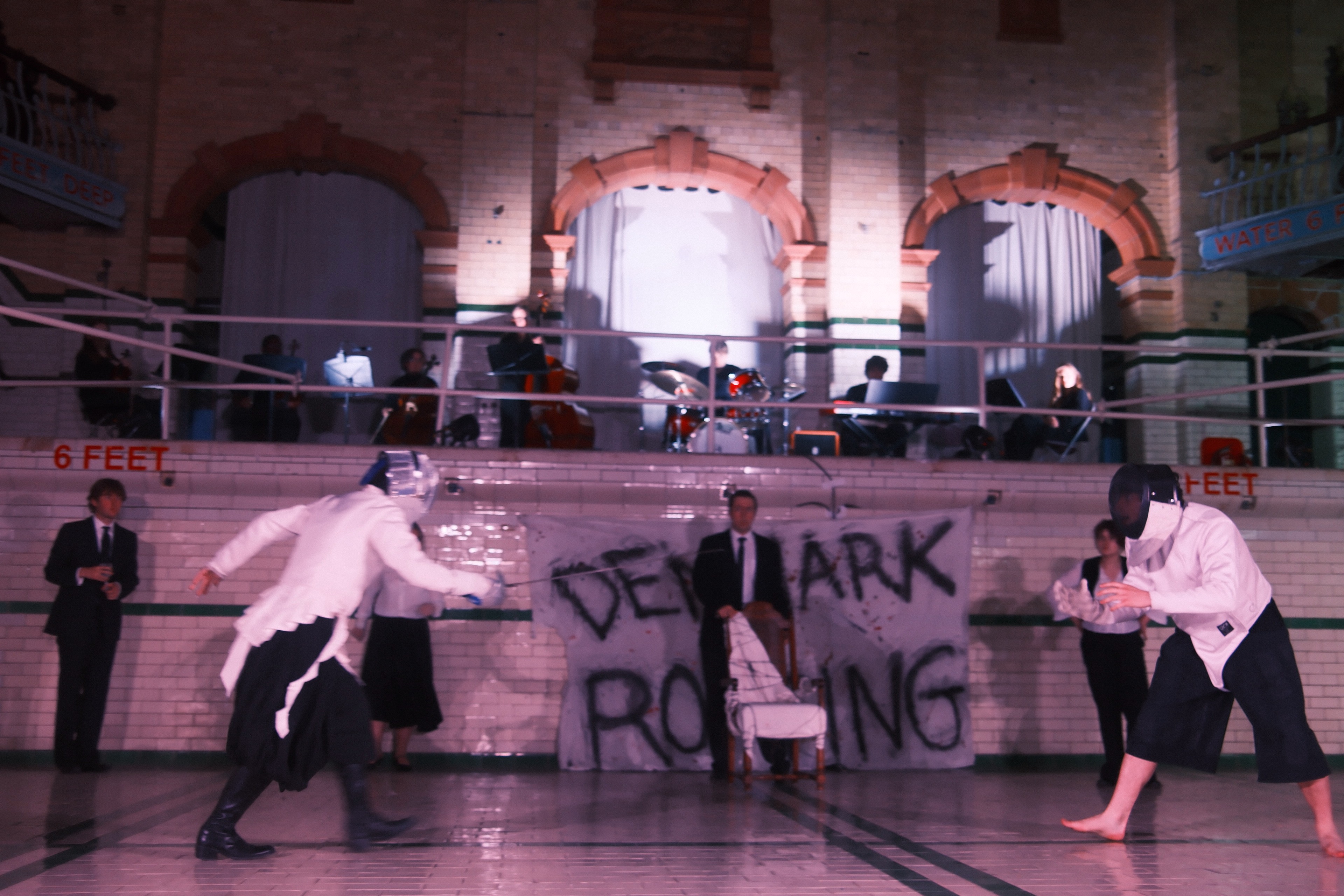 The final duel of Hamlet — masked fencers on the tiles beneath the balcony band.