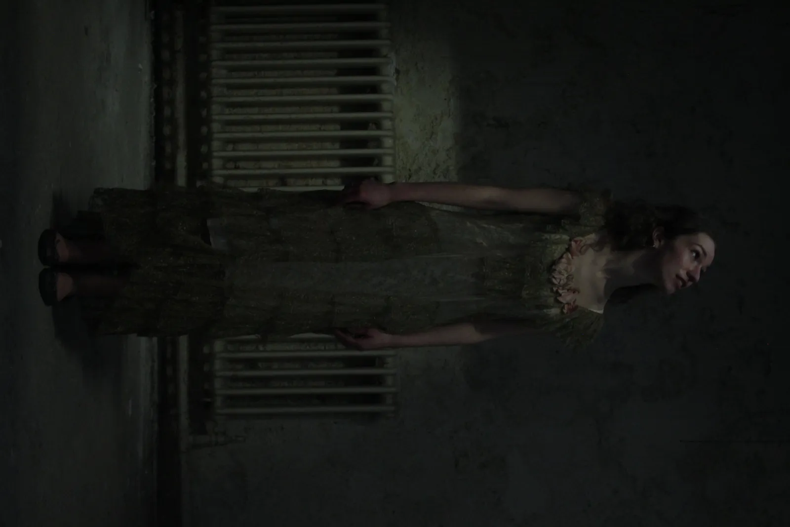 Promotional shot of Eurydice in her gown stretched along a radiator.