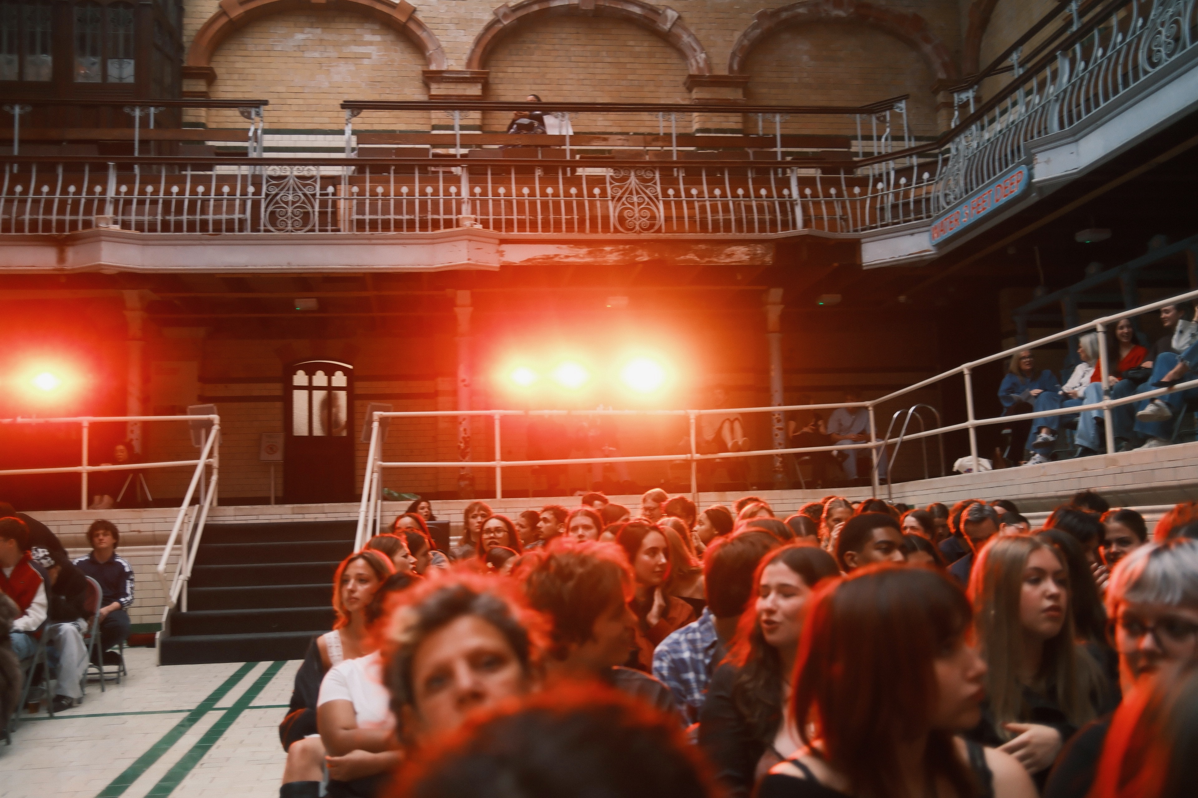 Audience inside the tiled hall of Victoria Baths, bathed in red front-light.
