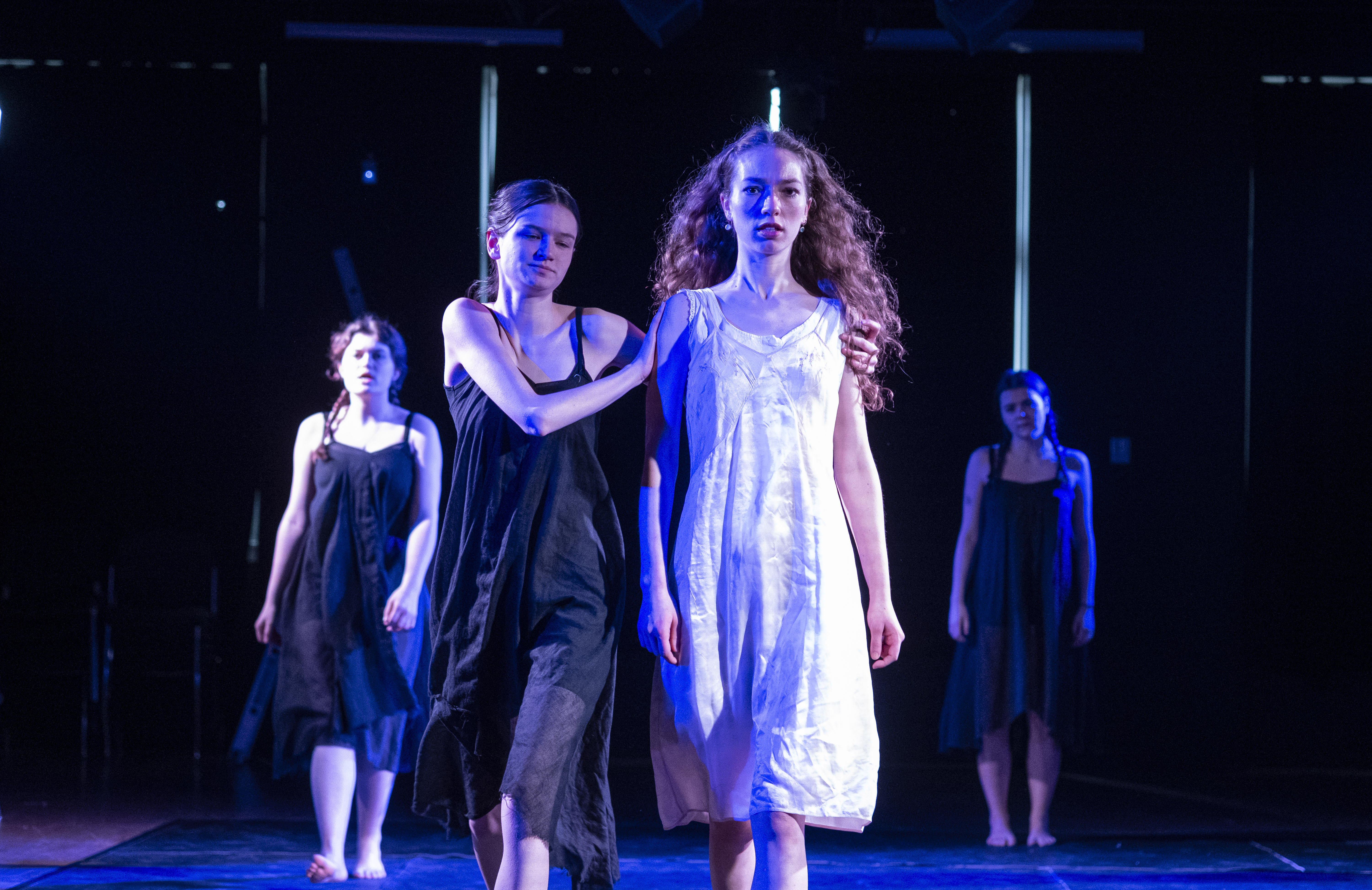 The ensemble huddled in the underworld under cold blue light.