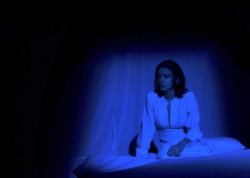 The Duchess seated at the head of her bed under a wash of blue.