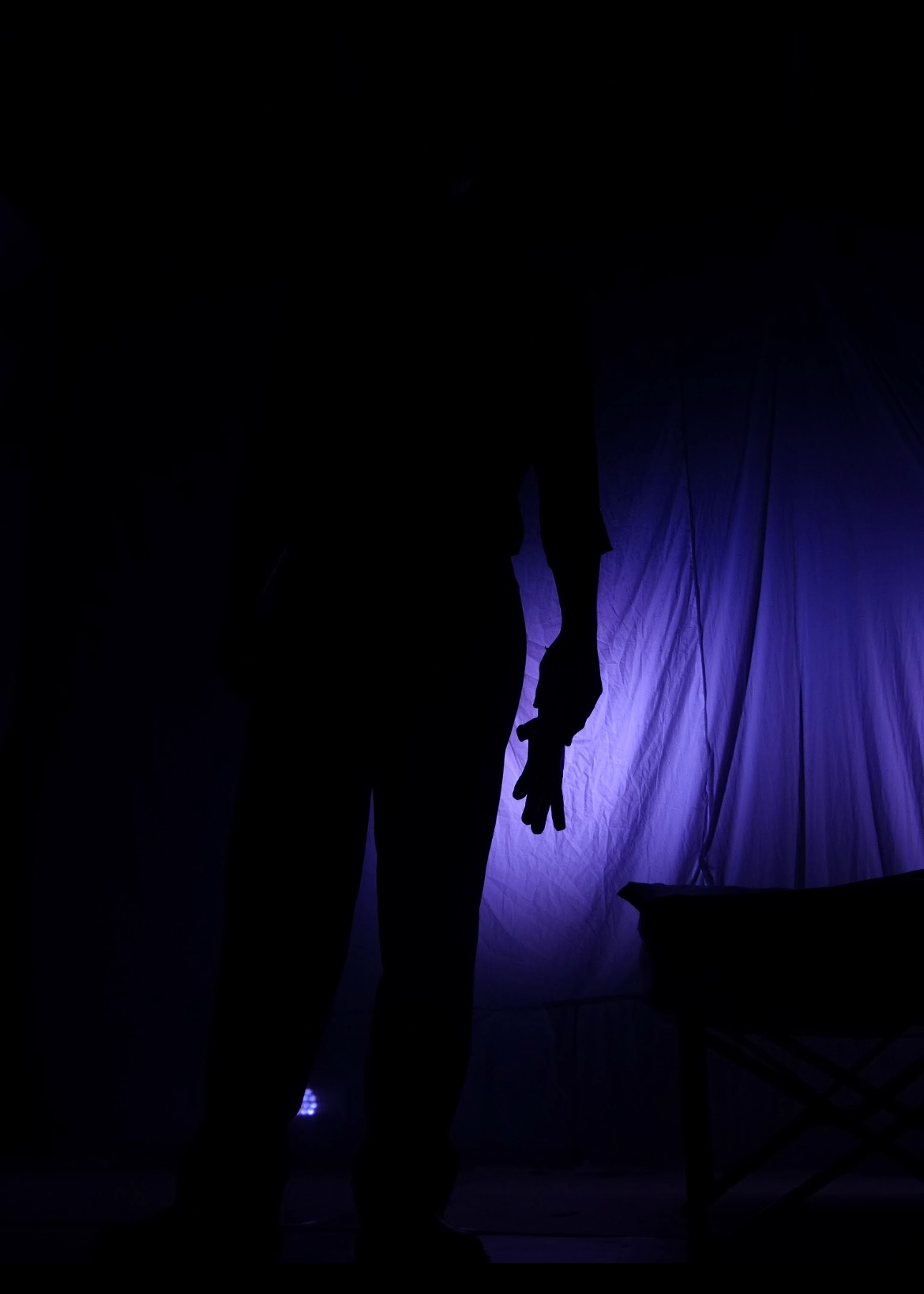 A silhouette hand reaches out against a violet-blue drape.