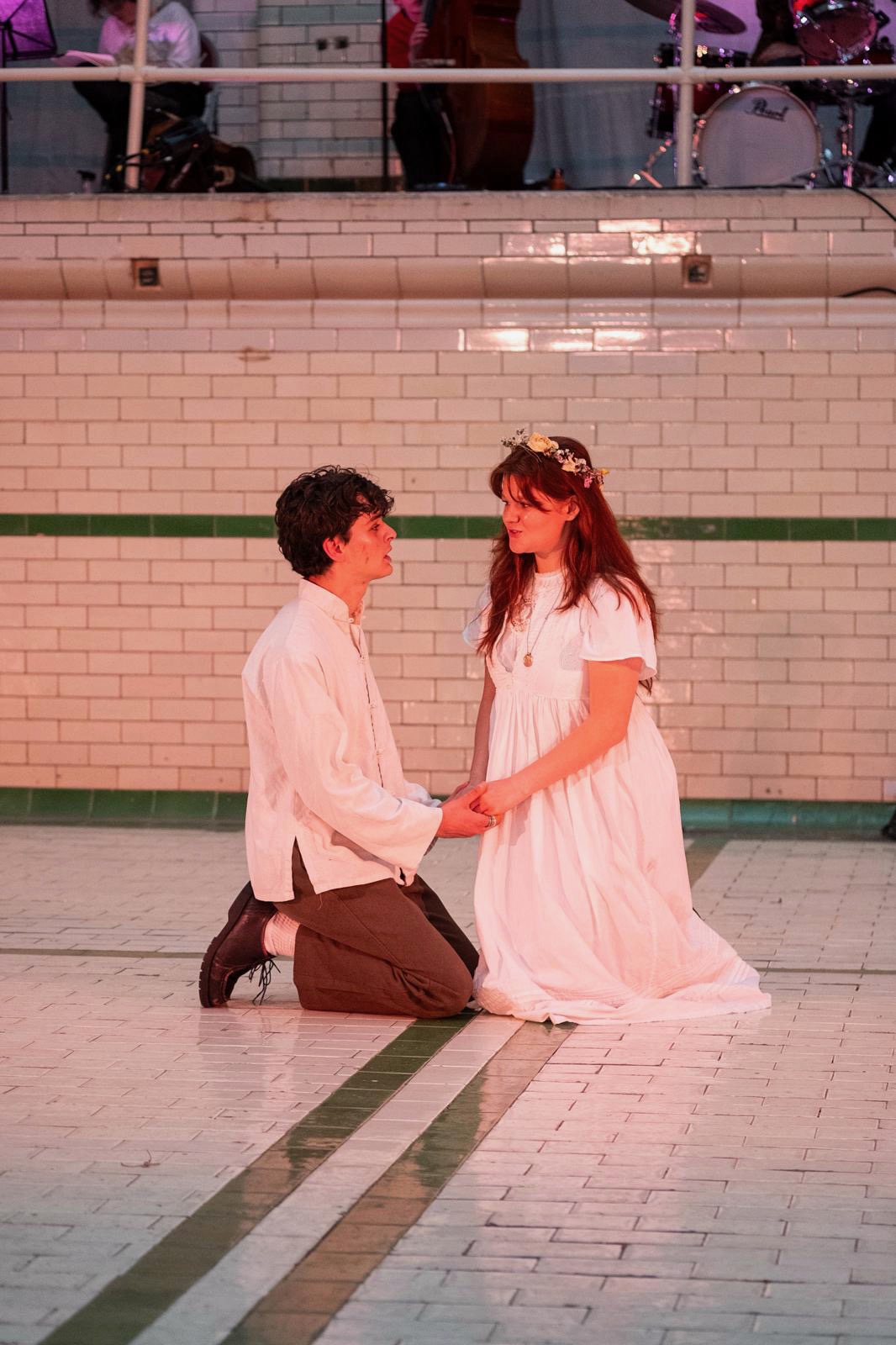 Romeo and Juliet kneeling at their wedding in warm tungsten light, band on the balcony.