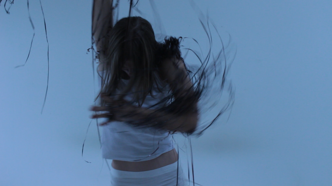 Figure in white spinning against a pale blue backdrop, hair caught in motion.