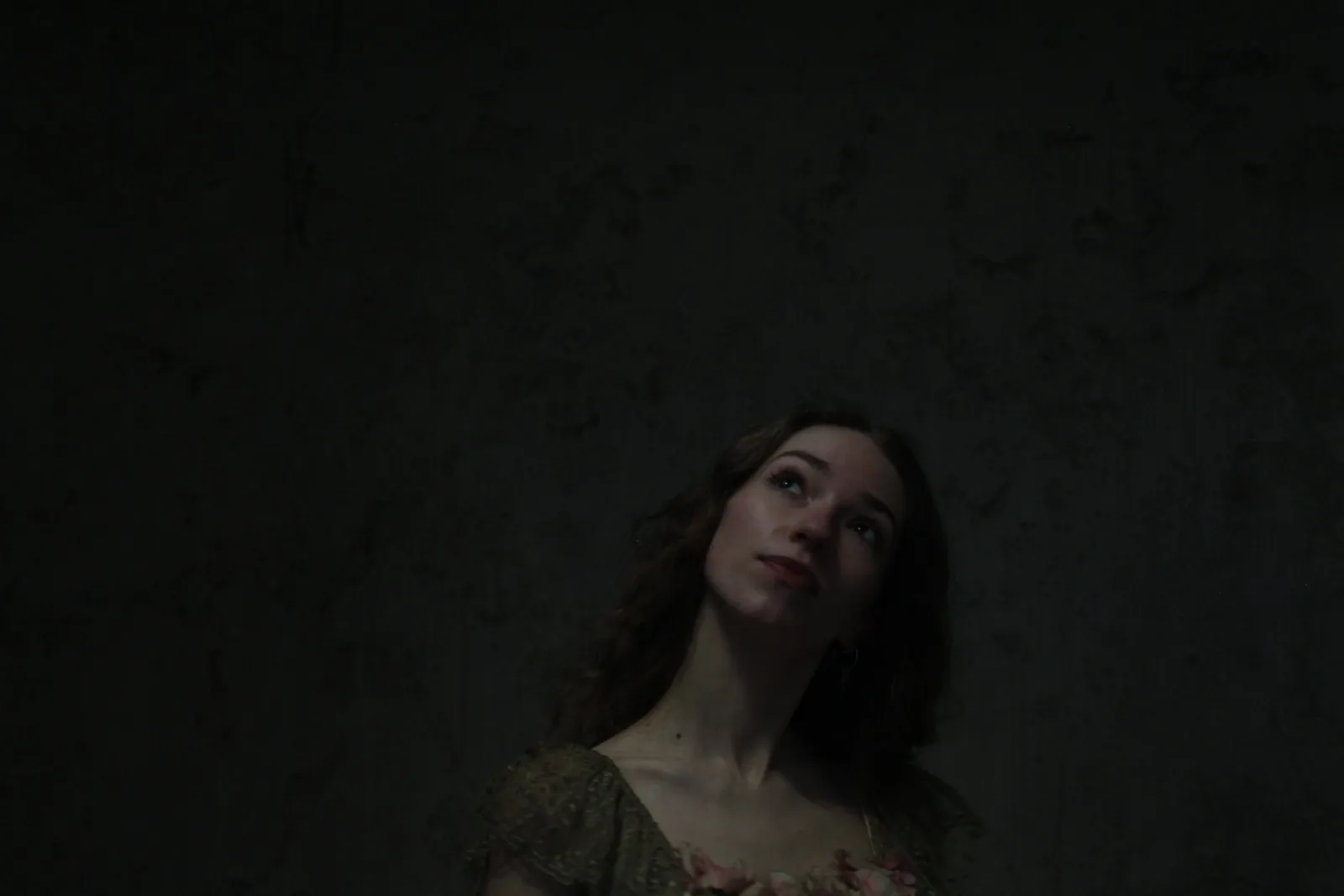 Eurydice in her gown looking upward in low light.