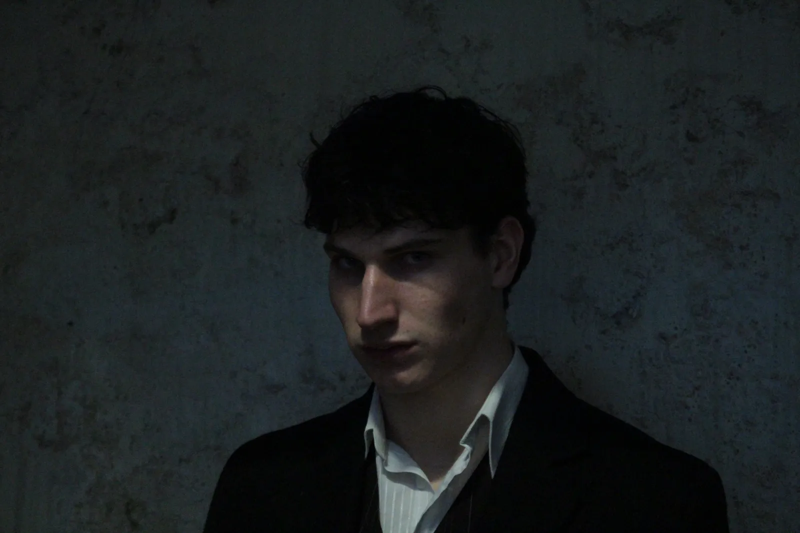 Promotional portrait, head turned to the side in low light.