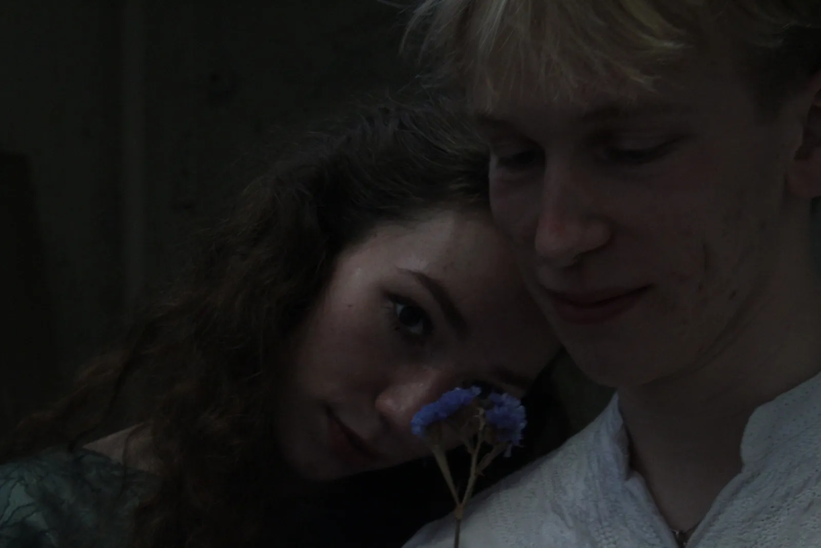 Eurydice and Orpheus cheek to cheek, holding a blue flower.
